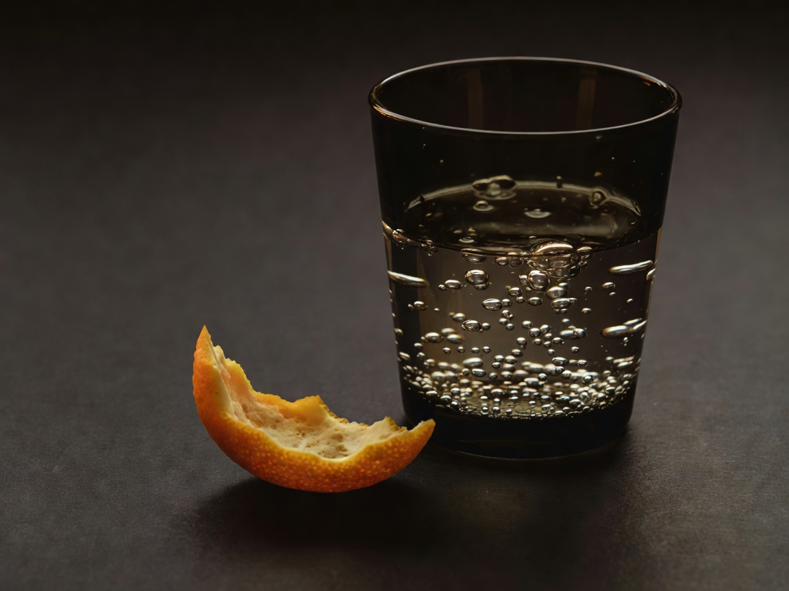 Citrus peel beside a glass of sparkling water in soft, dark lighting